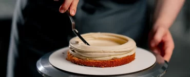close-up-female-baker-in-a-professional-kitchen-distributes-cream-onto-a-sponge-cake-with-a-spatula-1536x1024